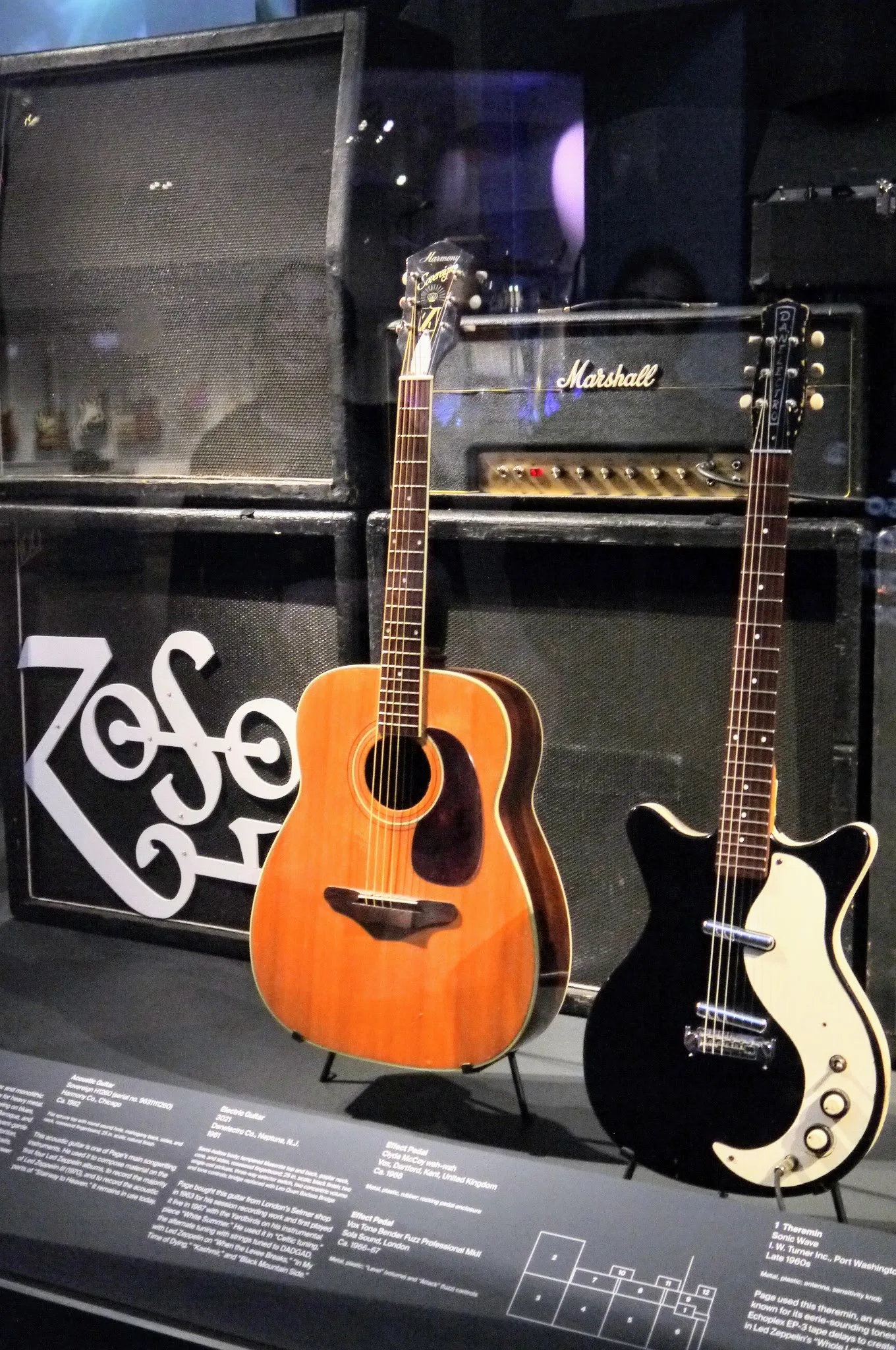 Две гитары на стойках перед стеной из усилителей Marshall и динамических кабинетов.